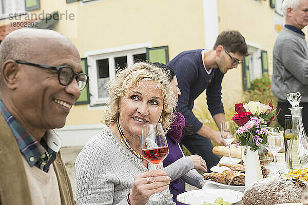 Ältere Frau lächelt mit einem Glas Wein und genießt eine Party im Freien mit ihrer Familie und Freunden auf einem Bauernhof in Bayern  Deutschland