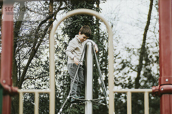 Seitenansicht eines Jungen oben auf einem Klettergerüst auf einem Spielplatz
