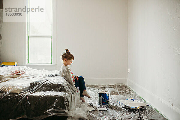Junges Mädchen sitzt auf dem Bett in einem frisch gestrichenen weißen Zimmer