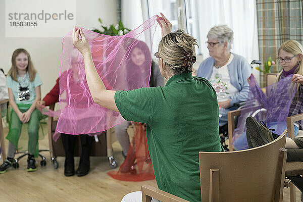 Mädchen mit Krankenschwester und ältere Frauen machen im Pflegeheim sanfte Sportübungen mit Stoff