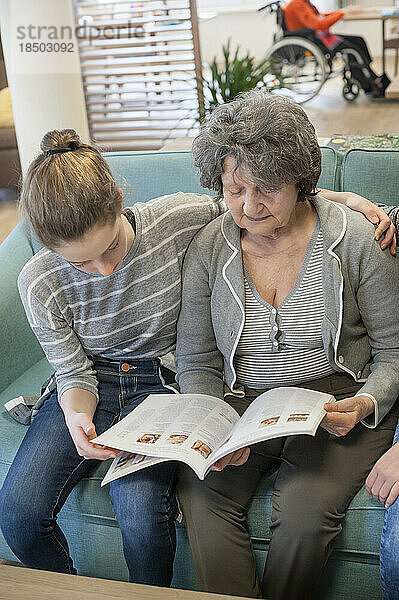 Mädchen lesen Zeitschrift mit Seniorin im Pflegeheim