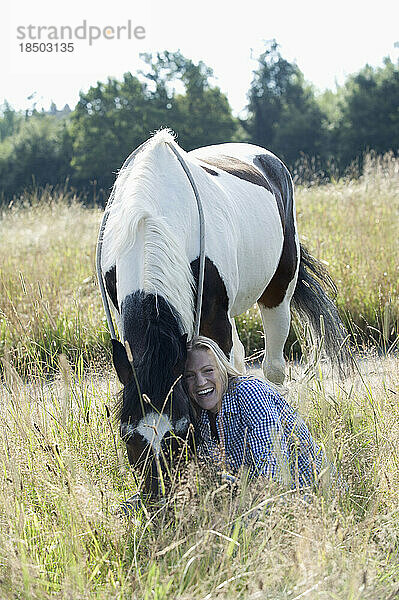 Mittlere erwachsene Frau streichelt ihr Pferd auf der Wiese und lächelt  Bayern  Deutschland