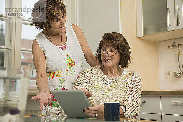 Zwei ältere Mitbewohner nutzen ein digitales Tablet und diskutieren etwas in der Küche  München  Bayern  Deutschland