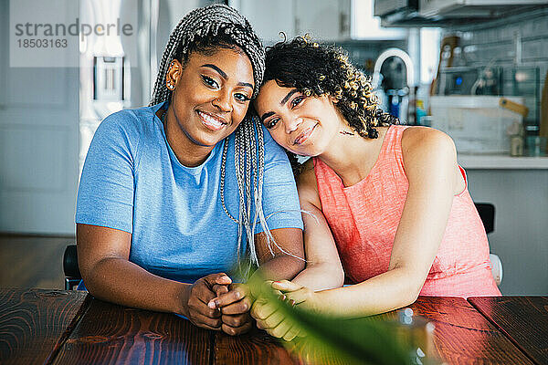 Porträt selbstbewusster  glücklicher Lesben  die am Tisch in der Küche sitzen