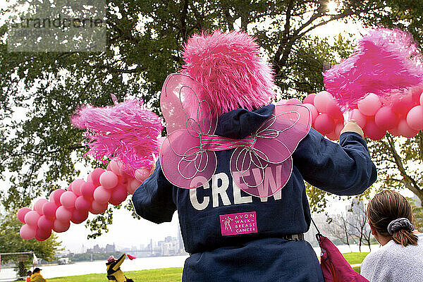 Crew member in pink wig cheers walkers during the Avon Walk for Breast Cancer in NYC.