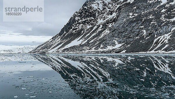 Ein teilweise schneebedeckter Berg spiegelt sich in den arktischen Gewässern
