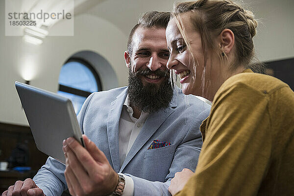 Fröhliches Paar lächelt  während es im Restaurant ein digitales Tablet benutzt