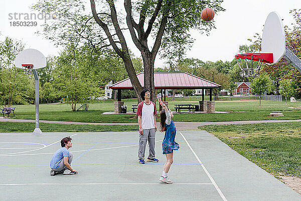 Ein Vater spielt im Frühling mit zwei Kindern im Park Basketball