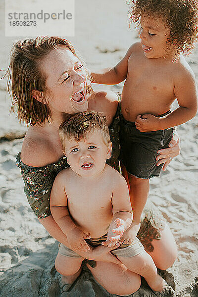 Lachende Mutter hält zwei kleine Jungen im Sand