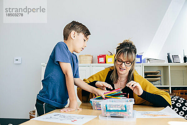 Der am Tisch sitzende Lehrer hilft dem Schüler beim Sortieren der Buntstifte