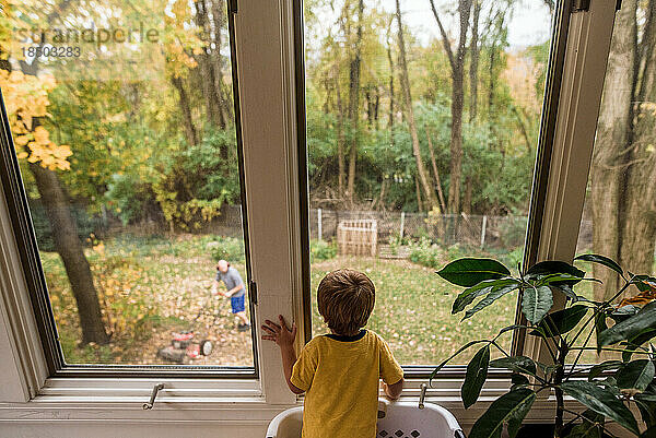 Junge schaut aus dem Fenster  während Papa Rasen mäht