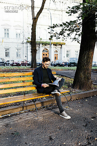 Stilvoller  lockiger Mann  der ein Buch liest  während er im Park sitzt