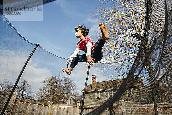 Ein glücklicher Junge macht draußen einen Split-Sprung auf dem Trampolin