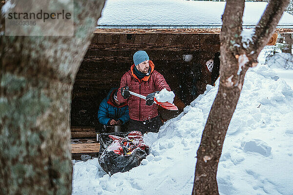 Mann schaufelt im Winter Schnee vor der Hütte
