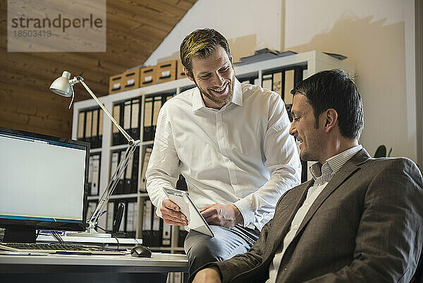 Zwei Geschäftsleute nutzen ein digitales Tablet in einem Büro und lächeln  Bayern  Deutschland