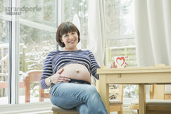 Porträt einer schwangeren Frau  die auf einem Stuhl sitzt
