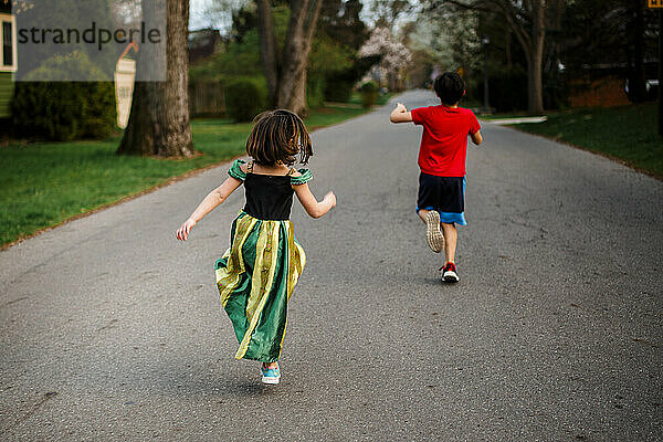 Zwei Kinder hüpfen im Frühling fröhlich eine von Bäumen gesäumte Straße entlang