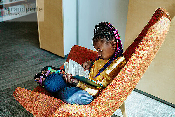 Afroamerikanisches Mädchen liest ein Buch auf einem Stuhl