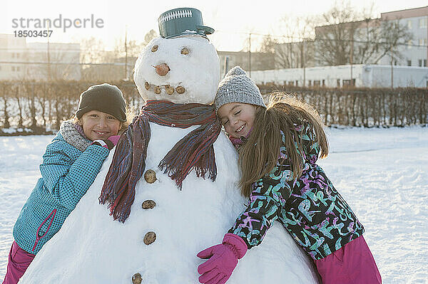 Zwei Mädchen stützen sich auf einen Schneemann