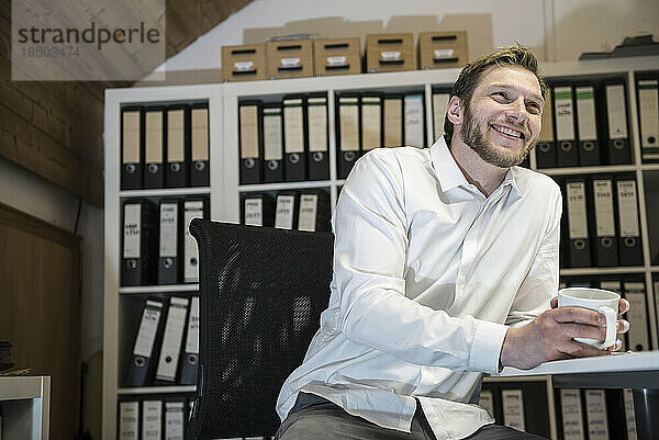 Mittlerer erwachsener Geschäftsmann  der in einem Büro Kaffee trinkt und lächelt  Bayern  Deutschland