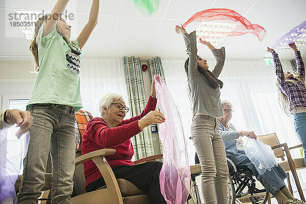 Mädchen und ältere Frauen machen im Pflegeheim sanfte Sportübungen mit Stoff