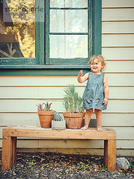Kleinkind steht auf Bank mit Topfpflanzen im Bauernhaushof.