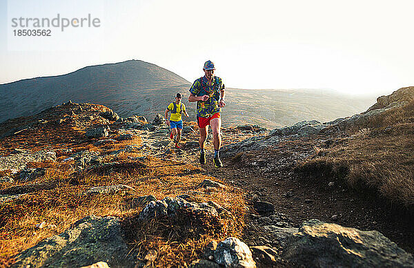 Männliche Trailrunner laufen bei Sonnenaufgang in den Bergen den Trail entlang