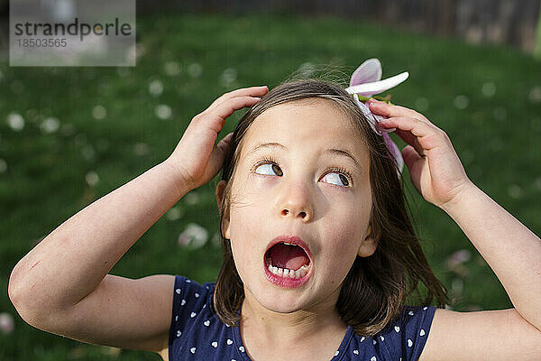 Ein kleines Mädchen hält an einem windigen Tag eine Blumenblüte als Hut auf dem Kopf