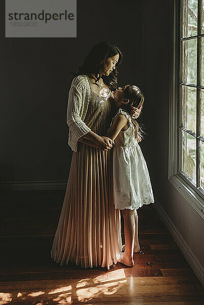Mother and daughter embrace and looking at each other by window