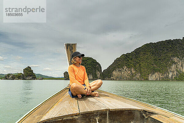 Lächelnde Frau sitzt in einem typischen thailändischen Boot und bewundert die Berglandschaft