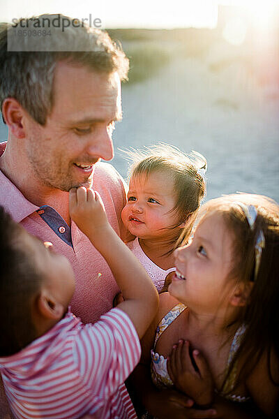 Nahaufnahme von Papa  der seine drei Kinder bei Sonnenuntergang am Strand von San Diego hält