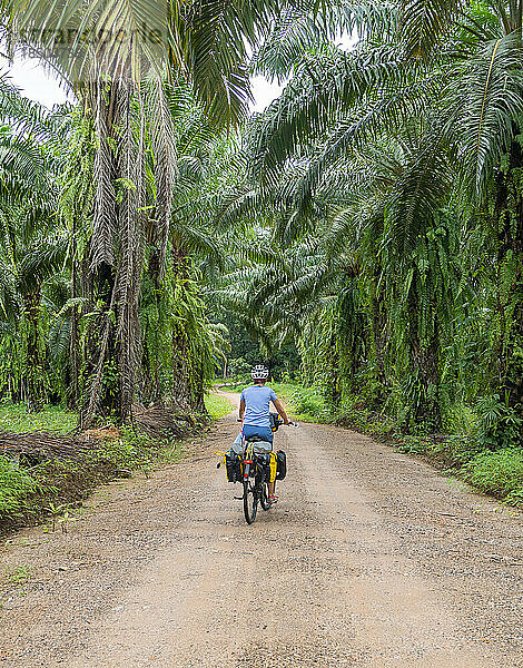 Bikepacking-Frau radelt auf unbefestigter Straße  umgeben vom thailändischen Dschungel