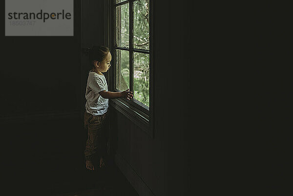 Preschool aged boy looking out the window at the trees