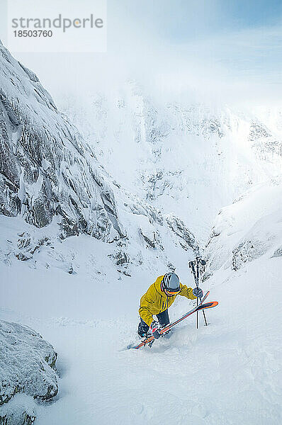Skifahrer in gelber Jacke klettert zurück zum Gipfel der Skipiste