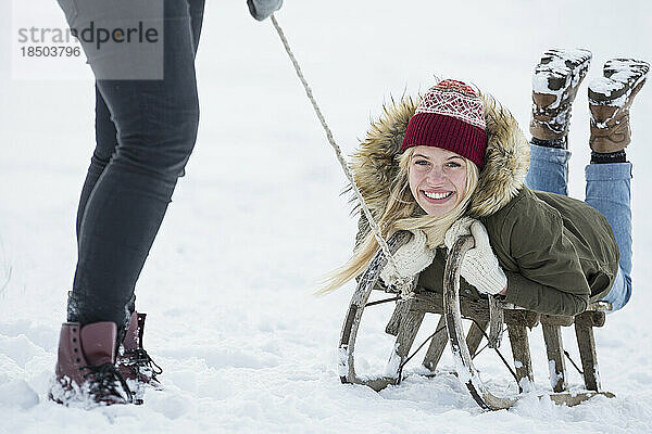 Zwei Mädchen im Teenageralter mit Rutsche in verschneiter Landschaft im Winter  Bayern  Deutschland