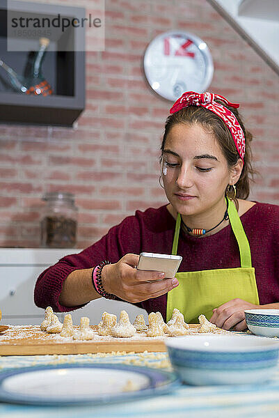 Teenager-Mädchen benutzt das Smartphone  während sie an traditioneller Arbeit arbeitet