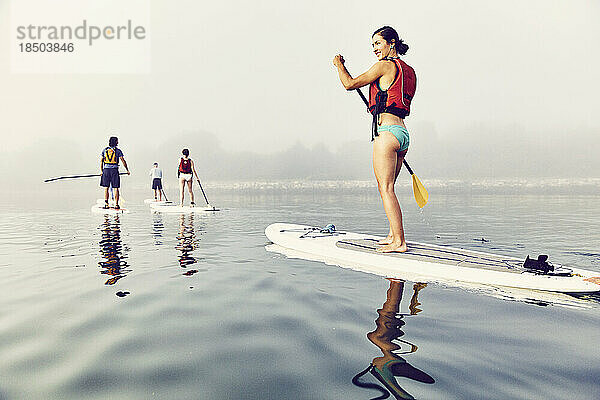 Eine Gruppe von Standup-Paddle-Boardern paddelt bei Sonnenaufgang im Nebel