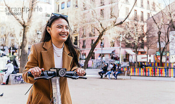 Asiatisches Mädchen  das städtisches elektrisches Skateboard benutzt