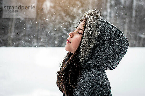 Mädchen steht friedlich draußen und fängt an einem Schneetag Schneeflocken