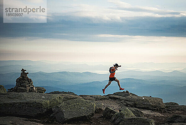 Trailrunner-Mann läuft entlang eines Bergrückens mit Steinhaufen und Bergen