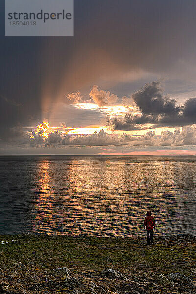 Mann steht und beobachtet den Sonnenaufgang an der bergigen Küste