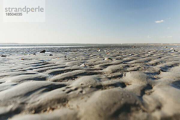 Tiefer Blick auf Wellen im Sand bei Ebbe am Strand mit blauem Himmel