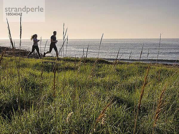 Mann und Frau laufen auf einem Singletrail am Strand von Azkorri