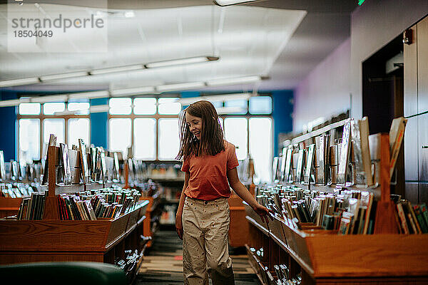 Glückliches junges Mädchen  das Bücher in einer Bibliothek betrachtet