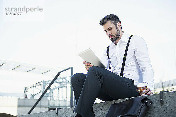 Geschäftsmann sitzt auf der Treppe und arbeitet mit Kaffee am digitalen Tablet  München  Bayern  Deutschland