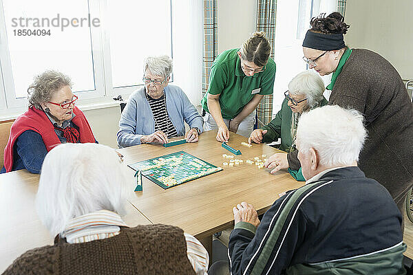 Senioren spielen Brettspiel mit Krankenschwester im Pflegeheim