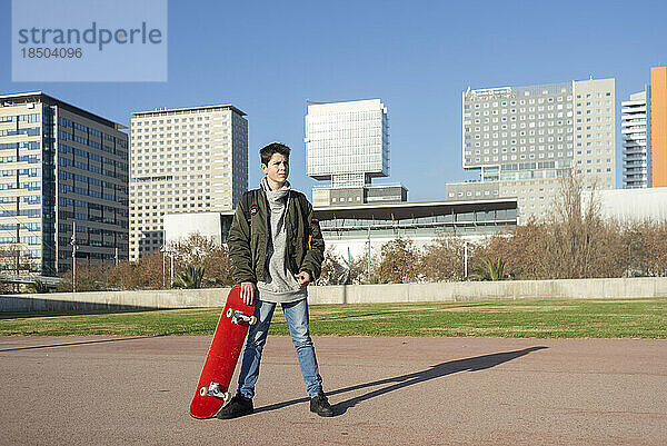 Aufnahme eines jungen Mannes  der draußen ein Skateboard hält.