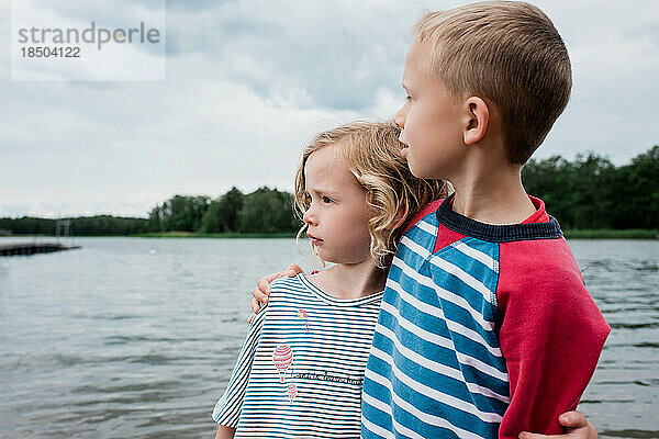 Bruder und Schwester umarmen sich und blicken im Sommer auf das Meer am Strand