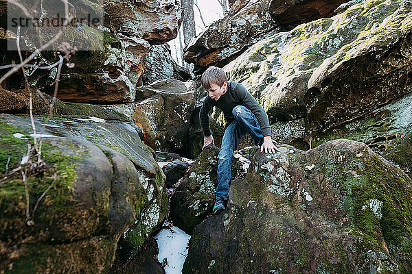 Junge klettert bei Wanderung im Wald über Felsen