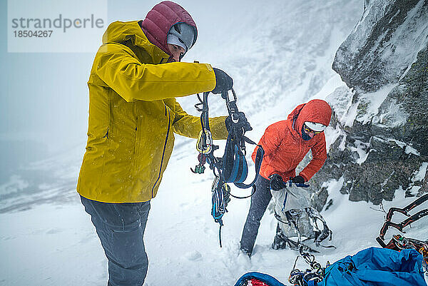 Männliche Kletterer ziehen Ausrüstung für Eisklettern im Schnee an